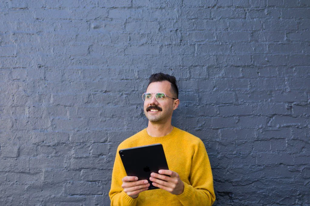 Jimmy Obomsawin wearing a yellow sweater, holding a tablet, and smiling
